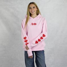 Alpha Phi hoodie in pink with super cute red hearts on the sleeve might just be the cutest design we carry this year. With the Alpha Phi Greek letters printed on the front and Alpha Phi since 1872 on the back it's a must-have addition to your wardrobe. With it's classic, unisex fit and a practical pouch pocket this versatile sweatshirt can be styled with everything on or off campus, whether studying, relaxing or hanging out with your sisters. Crafted from premium materials for comfort and warmth this sorority sweatshirt is perfect for layering or wearing on it's own. Part of our new 2024/2025 collection. Alpha Phi Hoodie Sizing Model is 5'9", size 0/2, and wearing size M A Phi Hoodie Technical Details  - Jersey lined hoodie  - Pouch pocket  - Unisex sizing  -  Sustainable Manufacturing  - Sorority Sweatshirts, Off Campus, Alpha Chi Omega, Womens Hoodies, Heart Hoodie, Alpha Chi, Sustainable Manufacturing, Lined Hoodie, The Alpha