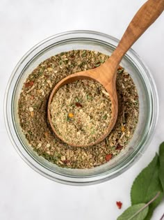 a wooden spoon in a glass bowl filled with spices and herbs on a white surface