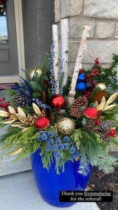 a blue vase filled with christmas decorations and greenery on the side of a house