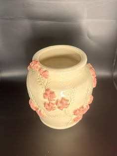 a white vase with pink flowers on it sitting on a black counter top in a display case