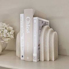 two books are sitting on a shelf next to a vase with white flowers in it