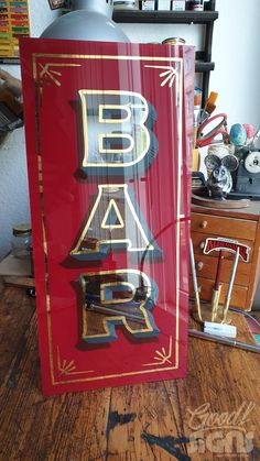 a red sign with gold lettering on it sitting on top of a wooden table next to a dresser