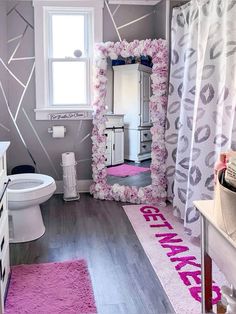 a bathroom decorated in pink and grey with flowers on the shower curtain, toilet seat cover, sink vanity and mirror