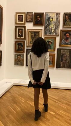 a woman standing in front of paintings on the wall and looking down at her skirt