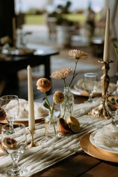 the table is set with candles, plates and flowers in glass vases on it