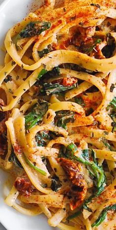 pasta with spinach and tomato sauce in a white bowl on top of a table