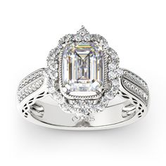 an emerald cut diamond surrounded by white diamonds in a halo style engagement ring with filigrees on the sides