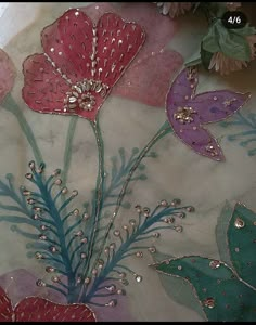 some flowers and leaves are on a table cloth with bead work in the middle