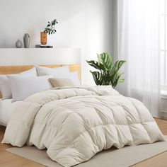 a bed with white comforters and pillows in a room next to a window,