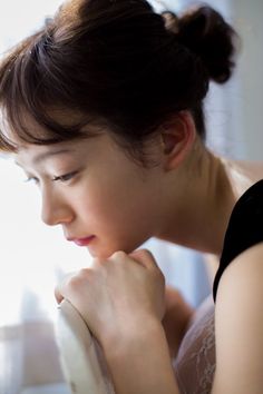 a woman is looking down while holding her hand near her face and wearing a black top