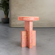 an orange table sitting on top of a cement floor next to a potted plant