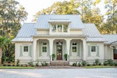 a white house with green shutters on the front and side windows, surrounded by trees