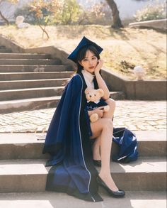 a young woman sitting on the steps with her teddy bear wearing a graduation cap and gown