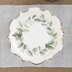 a white plate with green leaves on it sitting on top of a gray table cloth