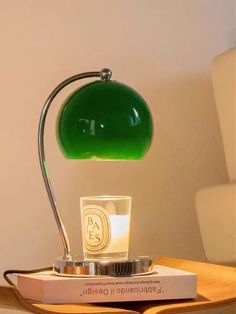 a green lamp sitting on top of a wooden table next to a glass cup and book