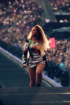 a woman with long hair walking on top of a stage in front of a crowd