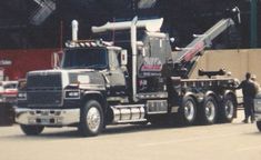 a large truck parked in a parking lot next to a man standing on the side of the road