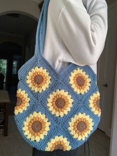 a woman is holding a crocheted bag with sunflowers on the front