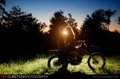 a person sitting on a motorcycle in the grass at night with their hand up to the camera