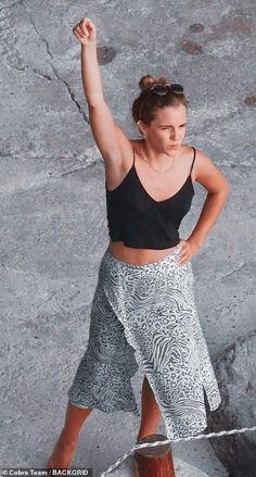 a woman standing on top of a rock with her arms in the air while wearing a skirt