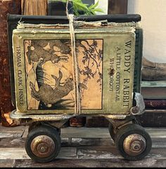 an old book is sitting on top of a small toy cart that has wheels attached to it