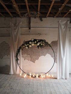 a circular wreath with flowers and candles is on the floor in front of white drapes