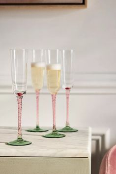 three wine glasses sitting on top of a white table next to a pink velvet chair