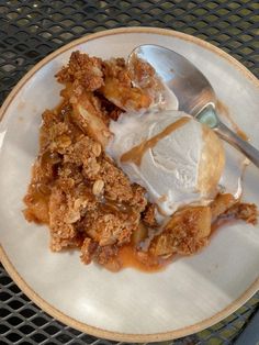 a white plate topped with an ice cream and apple crumbled dessert next to a spoon