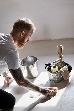 a man with tattoos is cleaning the floor in front of a bucket and pans