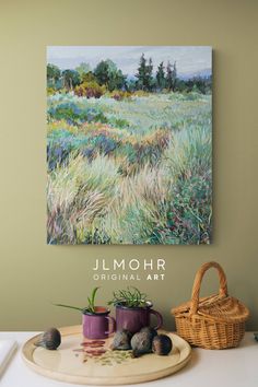 a painting hanging on the wall above a plate with two mugs and rocks in front of it