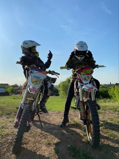 two people sitting on dirt bikes in the grass