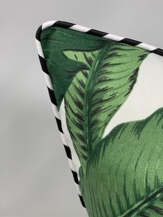 a green and white pillow with black stripes on the bottom, featuring a large leaf pattern