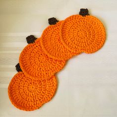 three orange crocheted pumpkin coasters sitting on top of a white tablecloth