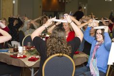 a group of people sitting at tables with their hands in the air while holding up remotes