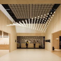 people are sitting at the reception desks in an empty room with lights hanging from the ceiling