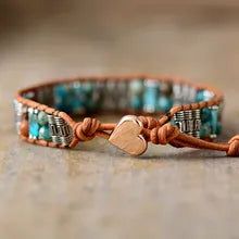 a leather bracelet with a heart charm on the clasp and beaded cord, sitting on top of a wooden table