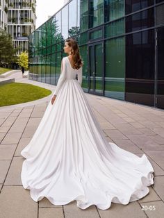 a woman in a white wedding dress is standing on the sidewalk with her back to the camera