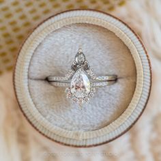 an engagement ring with a pear shaped diamond on it in a velvet display case, viewed from above