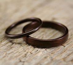 two wooden wedding rings sitting on top of a piece of wood with one ring in the middle