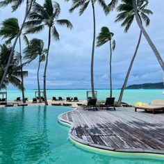 an outdoor swimming pool with lounge chairs and palm trees on the beach in front of it