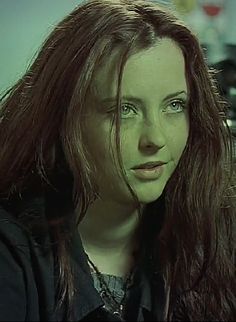 a woman with long red hair and green eyes looks at the camera while sitting down