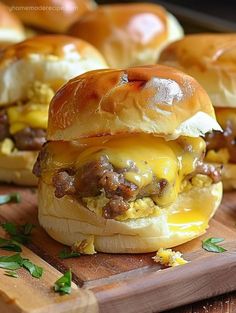 three cheeseburger sliders on a cutting board with other sliders in the background