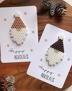 two greeting cards with christmas hats on them and pine cones in the background, one is made out of perforated paper