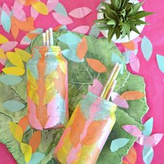 two painted mason jars sitting on top of a leafy green plate