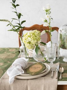 the table is set with plates, silverware and flowers in vases on it