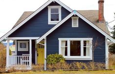 a blue house with white trim and yellow door on the front porch is surrounded by tall grass