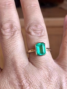 a woman's hand with a green ring on top of her finger and an emerald stone in the middle