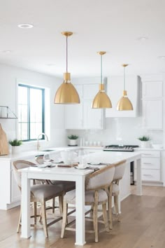 a kitchen with white cabinets and gold pendant lights hanging from the ceiling over a dining room table