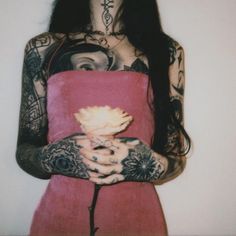 a woman with tattoos holding a flower in her hands