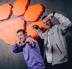 two men standing next to each other in front of a wall with the clemson logo on it